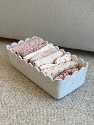 Set of pink fabric rolls in a decorative white container on a beige surface.