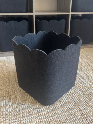 A Dark Gray scalloped storage bin placed on a wooden floor, with a modern and sleek design.