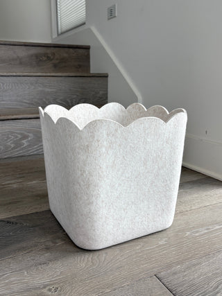 A beige scalloped storage bin placed on a wooden floor, with a modern and sleek design.