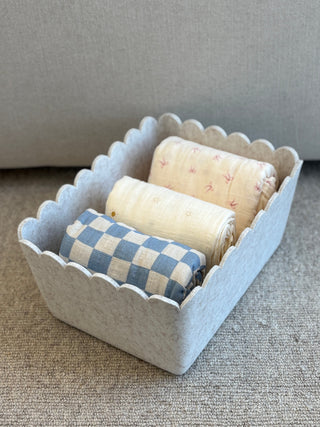 Wide decorative basket with rolled-up fabric rolls on a textured surface