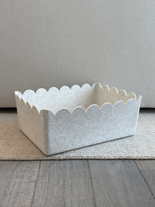 Beige scalloped-edge storage basket on a wooden floor with a neutral background