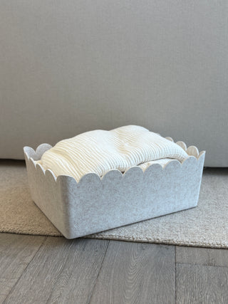 Beige scalloped-edge box with a stack of white towels on a gray surface.